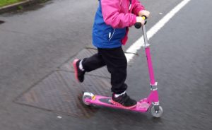 girl riding scooter across road